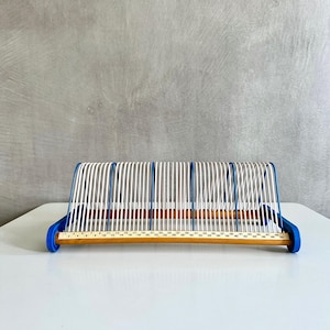May include: A wooden and metal document holder with a blue base and white vertical supports. The base has a ruler printed on it, with measurements up to 127 cm. The document holder is designed to organize papers.