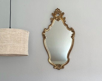 May include: A gold ornate mirror with a decorative frame and a beveled glass surface.