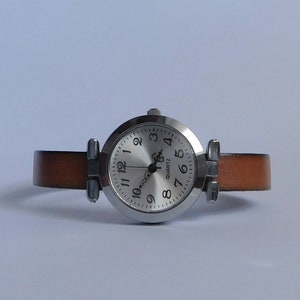 May include: A silver wristwatch with a white face and black numbers. The watch has a brown leather band.