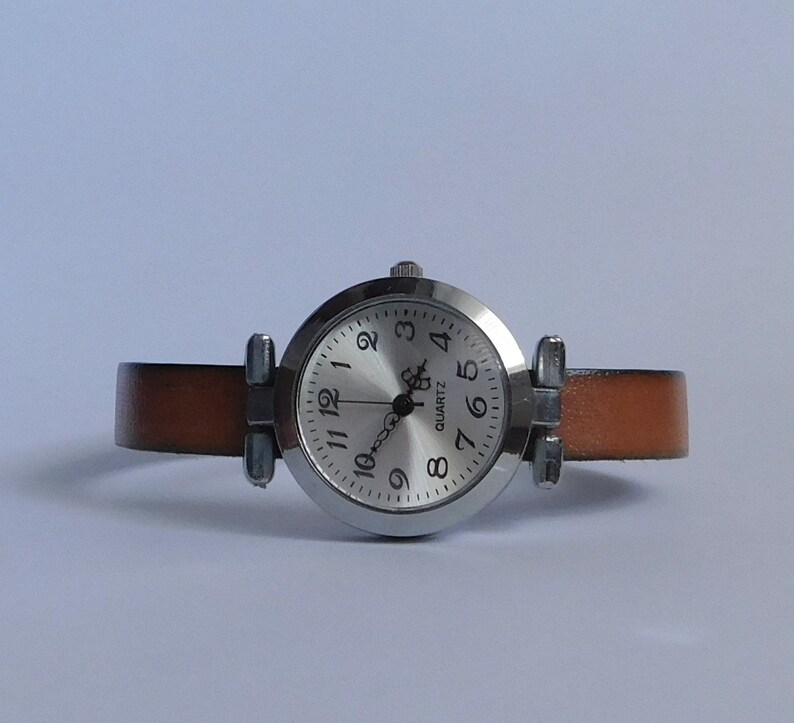 May include: A silver wristwatch with a white face and black numbers. The watch has a brown leather band.