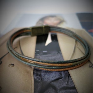 May include: A triple-wrap leather bracelet with a dark green and brown color scheme. The bracelet has a simple, minimalist design.