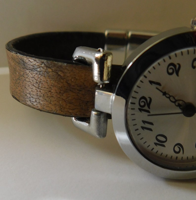May include: A silver wristwatch with a brown leather band. The watch face has black numbers and a silver second hand.