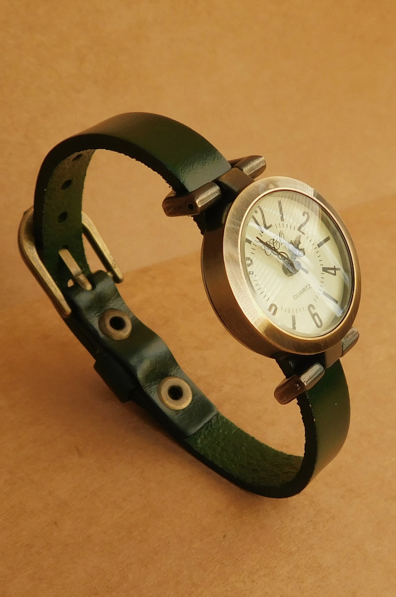 This is a wristwatch round shape 1 inch diameter, 
made in alloy, aged bronze finish, free of nickel and lead.
Analog, quartz, battery operated (new battery inside).
The wristband is made with green leather 
and fit from 6.25 to 7.25 inches wrist.