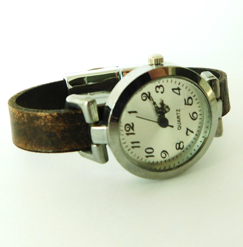 May include: A silver wristwatch with a brown leather band. The watch face is white with black numbers and hands. The watch face also says "QUARTZ".