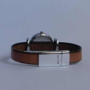 May include: A brown leather watch band with a silver clasp and a round silver watch face.