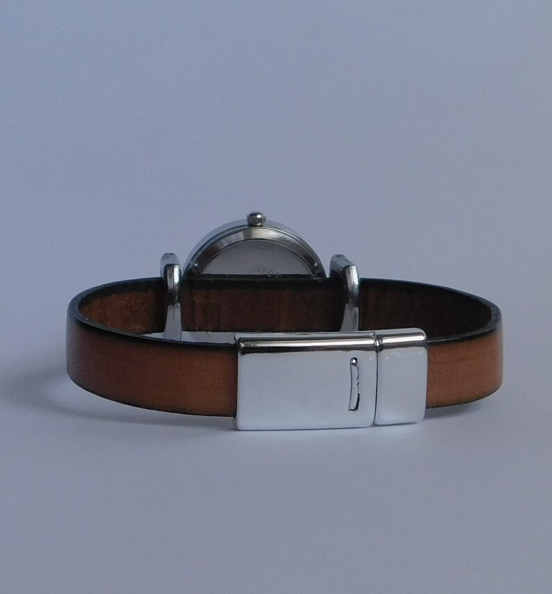 May include: A brown leather watch band with a silver clasp and a round silver watch face.