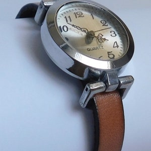 May include: A silver wristwatch with a white face and black hands. The watch has a brown leather band and says "QUARTZ" on the face.