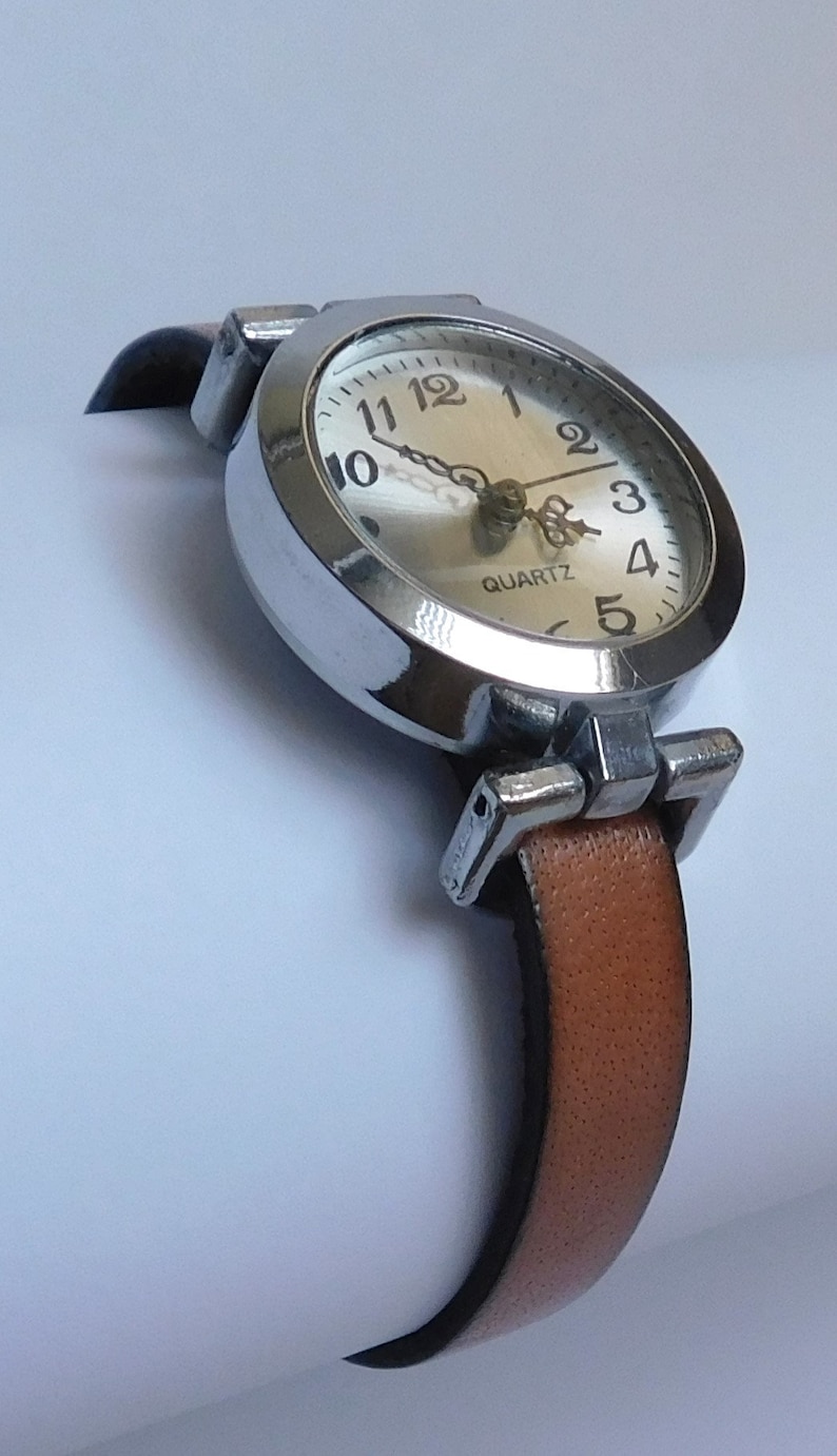 May include: A silver wristwatch with a white face and black hands. The watch has a brown leather band and says "QUARTZ" on the face.