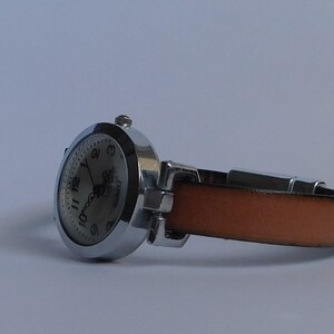 May include: A silver wristwatch with a white face and black numbers. The watch has a brown leather band.