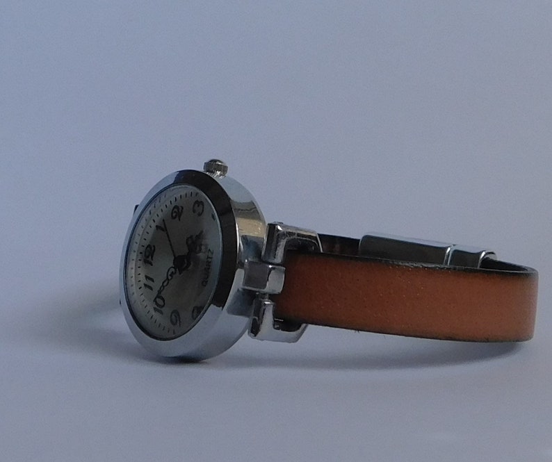 May include: A silver wristwatch with a white face and black numbers. The watch has a brown leather band.