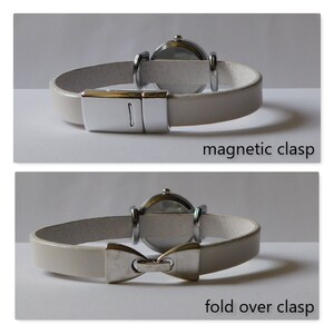 May include: Two white leather watch bands with different clasps. The top band has a magnetic clasp. The bottom band has a fold over clasp.