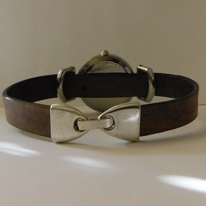 May include: A brown leather watch band with a silver buckle and a round silver watch face.