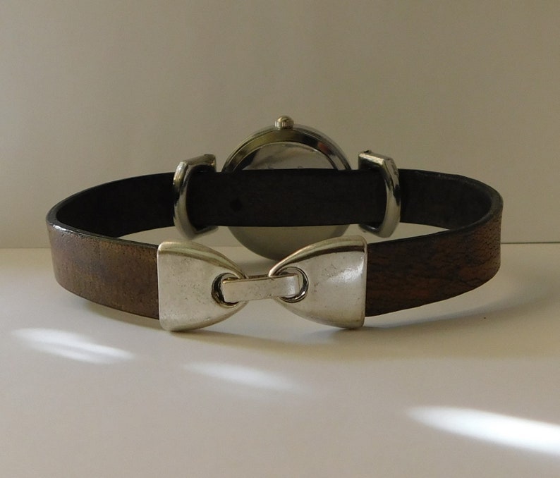 May include: A brown leather watch band with a silver buckle and a round silver watch face.