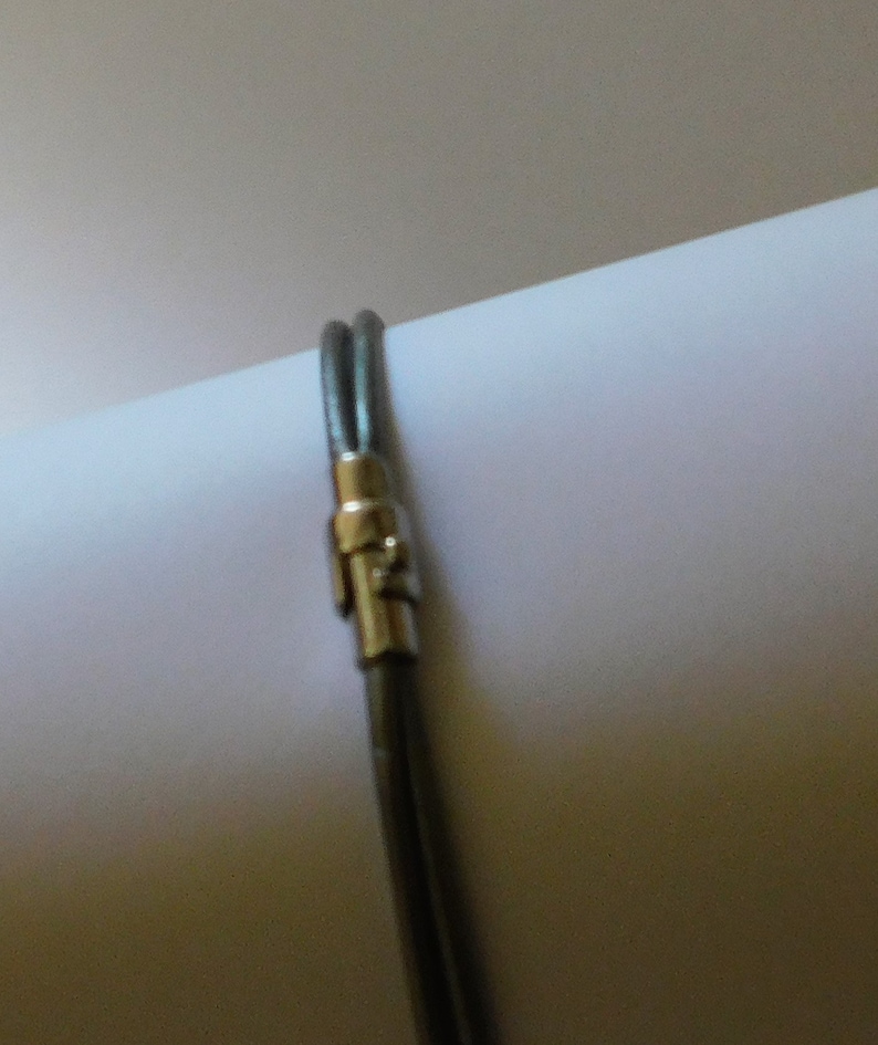 May include: A double-strand dark gray leather bracelet featuring a polished silver-tone metal cylindrical clasp. The two thin leather cords are secured together by the metallic fastener, creating a simple and clean design for the wrist.