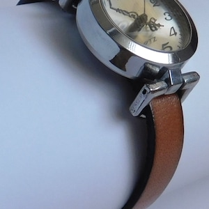 May include: A silver wristwatch with a white face and black hands. The watch has a brown leather band.
