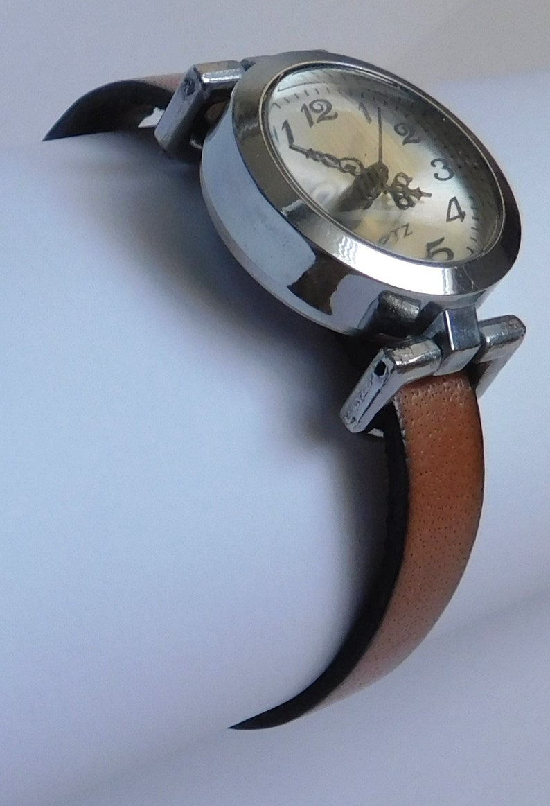 May include: A silver wristwatch with a white face and black hands. The watch has a brown leather band.