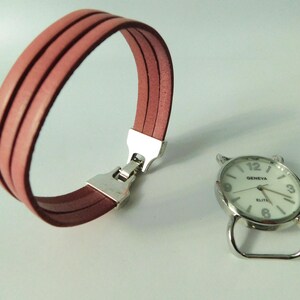 Puede incluir: Una pulsera de tres hilos en color rosa empolvado con un cierre de metal plateado y una esfera de reloj redonda plateada por separado con fondo blanco, que muestra el texto Geneva Elite, n&uacute;meros negros y manecillas plateadas, sin correa.