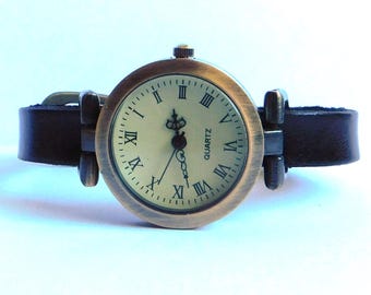 May include: A vintage-style quartz watch with a round, bronze-colored case and a cream-colored face featuring Roman numerals. The watch has a black leather band. The watch face reads "QUARTZ".