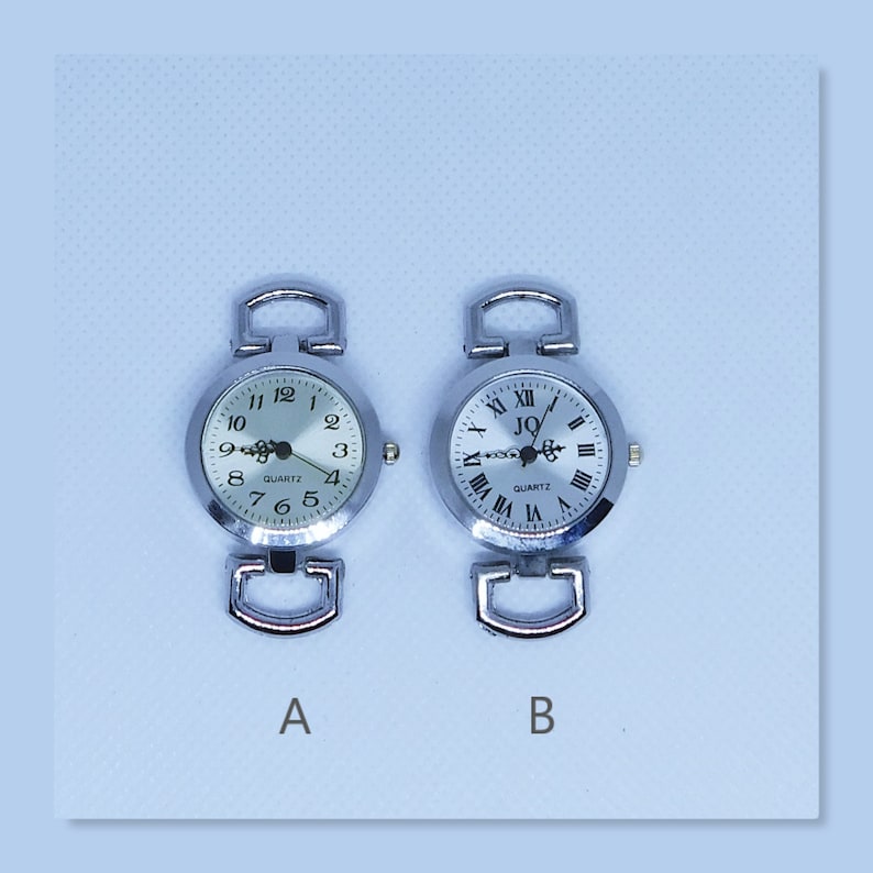 May include: Two silver wristwatches with white faces and black Roman numeral hour markers. The watch on the left has black Arabic numeral minute markers. The watch on the right has a black logo that says "JQ" and the word "QUARTZ" printed below it. Both watches have silver bands.