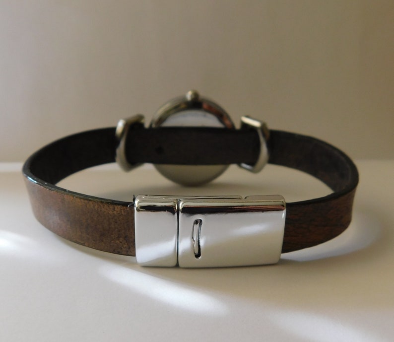 May include: A brown leather watch band with a silver clasp and a round watch face.