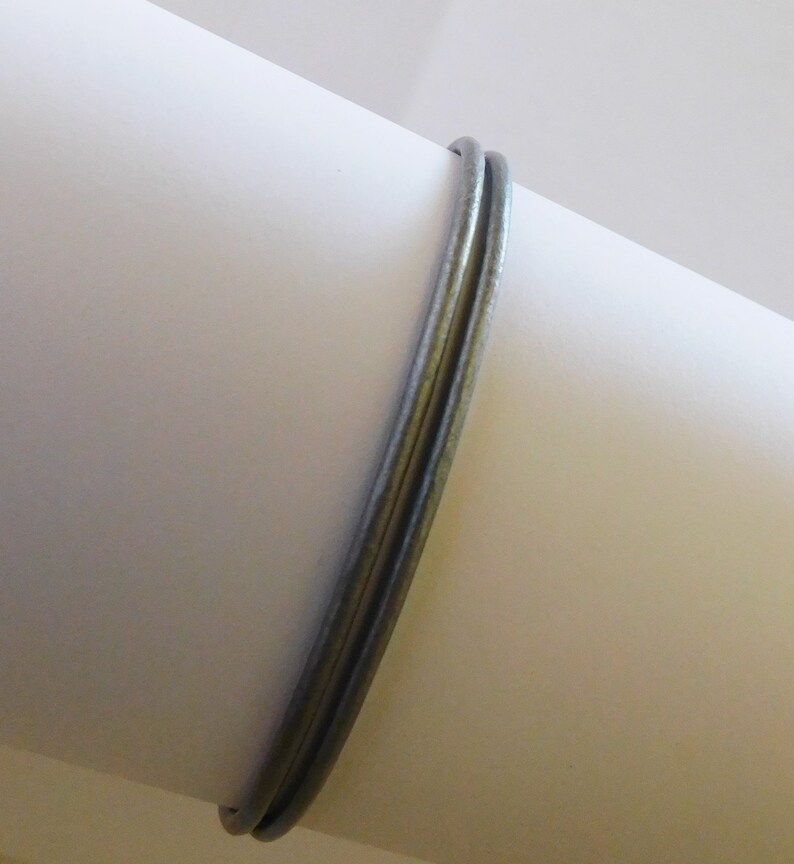 May include: A double-layered bangle bracelet crafted from a smooth, matte-finished silver-toned metal. The two thin, circular bands are joined together to form a single piece of jewelry with a consistent, uniform thickness and a neutral metallic color.