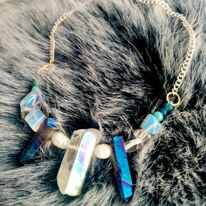 Pode incluir: Um colar de corrente de prata com detalhes de cristal iridescente e pérolas. O colar apresenta uma variedade de formas de cristal, incluindo cristais longos e finos e pérolas redondas.