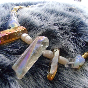 Pode incluir: Um colar com cristais iridescentes e detalhes dourados. Os cristais são facetados e têm um brilho arco-íris. O colar é enfiado em um cordão transparente com contas brancas.