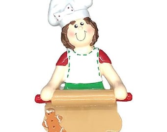 May include: A white chef hat with red polka dots on top of a girl's head. She is wearing a red and green shirt and a white apron. She is rolling out dough with a rolling pin. There is a gingerbread cookie on the dough.