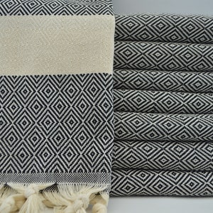 May include: A stack of white and black patterned Turkish towels with fringe. The towels are folded and stacked on top of each other.