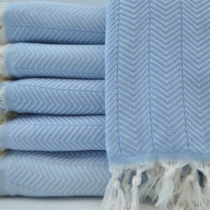 May include: A stack of light blue towels with a white chevron pattern and white fringe.