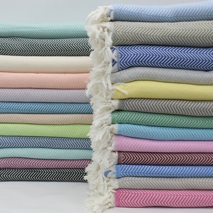 May include: A stack of colorful woven cotton throws with a herringbone pattern. The throws are folded and stacked in a variety of colors, including pink, blue, green, and yellow.
