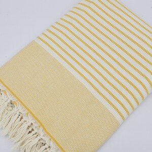 May include: A yellow and white striped Turkish towel with fringe. The towel is made of cotton and is soft and absorbent.