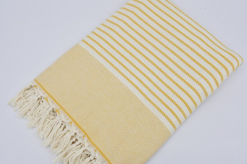 May include: A yellow and white striped Turkish towel with fringe. The towel is made of cotton and is soft and absorbent.