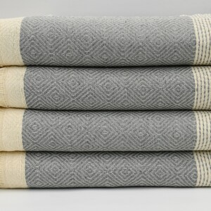 May include: A stack of four gray and white patterned Turkish towels with fringed edges.