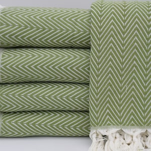 May include: A stack of four green and white chevron patterned throw blankets with white fringe.