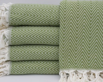May include: A stack of four green and white chevron patterned throw blankets with white fringe.