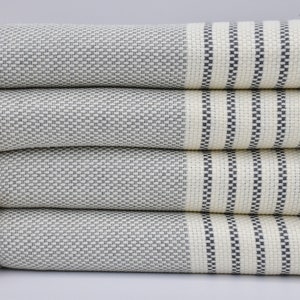 May include: Four white towels with gray stripes stacked on top of each other. The towels have a fringe on one side.
