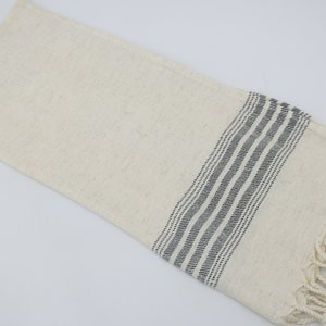 May include: A white cotton towel with black stripes and fringe.