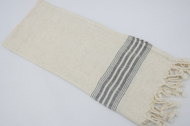 May include: A white cotton towel with black stripes and fringe.