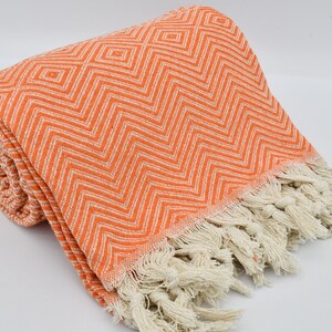 May include: Orange and white patterned throw blanket with fringe. The blanket is made of cotton and is soft and absorbent.
