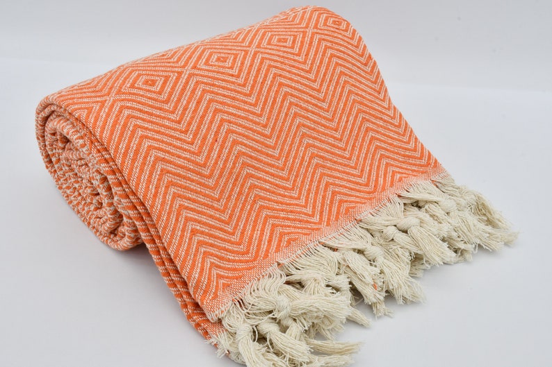 May include: Orange and white patterned throw blanket with fringe. The blanket is made of cotton and is soft and absorbent.
