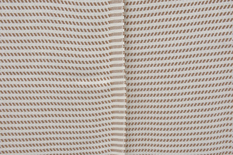 K&ouml;nnte beinhalten: Nahaufnahme eines wei&szlig;en Stoffes mit braunem diagonalem Streifenmuster. Der Stoff hat eine subtile Textur und ein leicht raues Gef&uuml;hl.