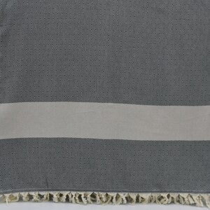 May include: A gray and white striped Turkish towel with a diamond pattern. The towel has a fringe border.
