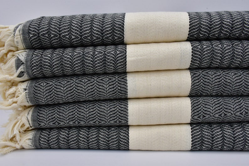 K&ouml;nnte beinhalten: Ein Stapel aus f&uuml;nf schwarzen und wei&szlig;en gestreiften Handt&uuml;chern mit Fransen an den R&auml;ndern. Die Handt&uuml;cher sind aus einem weichen, saugf&auml;higen Material gefertigt und eignen sich perfekt zum Abtrocknen nach dem Duschen oder Baden.