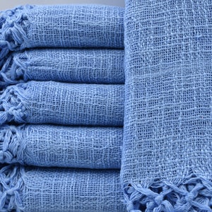 May include: A stack of light blue woven cotton throws with fringed edges.