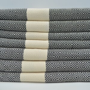 May include: A stack of eight white and black patterned towels with fringe edges. The towels are folded and stacked on a white surface.