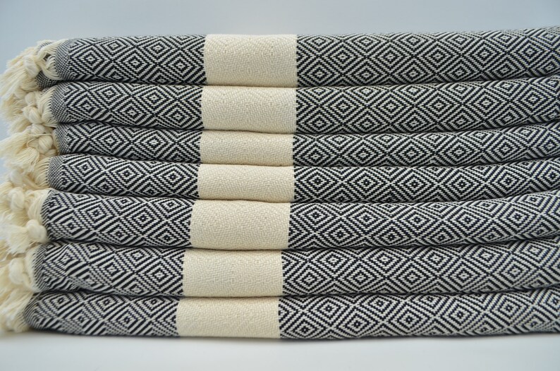 May include: A stack of eight white and black patterned towels with fringe edges. The towels are folded and stacked on a white surface.