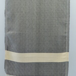 May include: A black and white patterned Turkish towel with a cream colored stripe and fringe on the bottom.