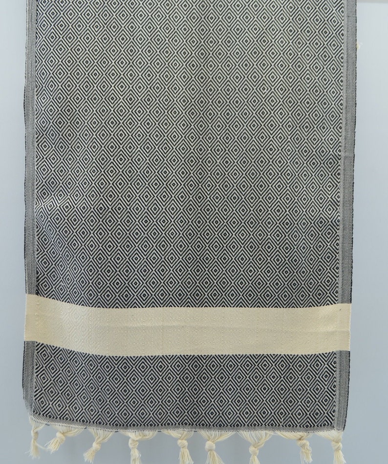 May include: A black and white patterned Turkish towel with a cream colored stripe and fringe on the bottom.