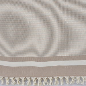 K&ouml;nnte beinhalten: Ein beige-wei&szlig; gestreiftes t&uuml;rkisches Handtuch mit Fransenrand. Das Handtuch hat eine dezente gewebte Textur.
